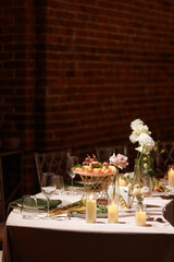 Wedding banquet table decorated with candles, flowers and food in elegant restaurant interior with brick wall. Concept of celebration, romance, reception, event decoration.