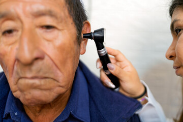 Doctor examining senior man's ear with otoscope during medical consultation