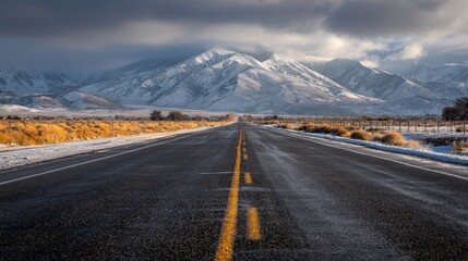 Scenic empty asphalt road leading toward majestic snow-covered mountain range under clear blue sky, picturesque winter travel landscape with open highway surrounded by natural wilderness and alpine sc