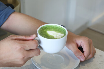 Close Up Man Hand Holding Green Matcha Latte Art in Mug
