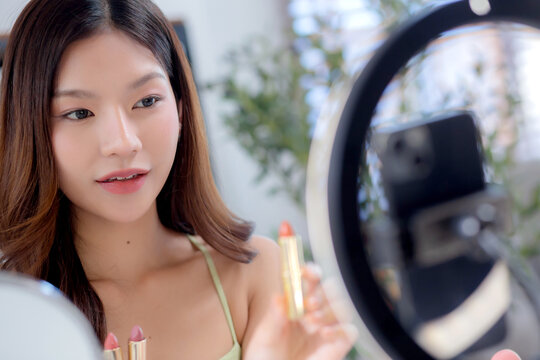 Young asian beauty influencer testing multiple lipstick shades on arm while recording makeup review at home, cosmetic product of content creator on social media and presenting, beauty and care.