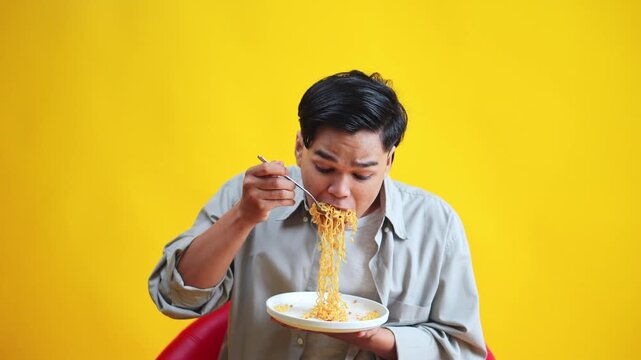 Casual young man happily and intently slurping noodles isolated on yellow background