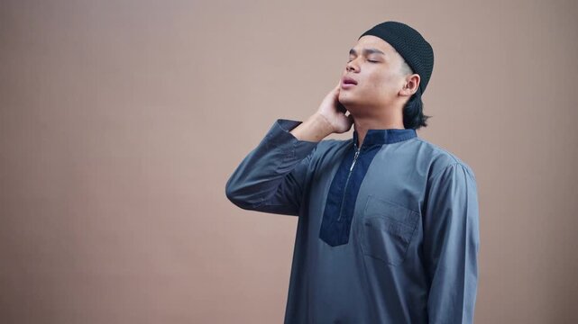 Young Muslim man praying with eyes closed and hand on neck seeking divine connection and peace. Doing Adzan