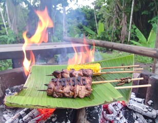 Grilled skewers on banana leaf over fire