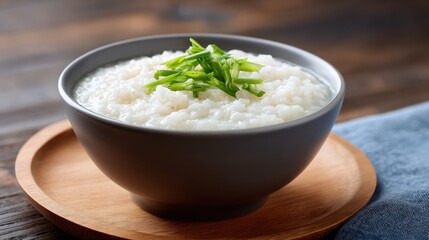Close-up of a black ceramic bowl filled with creamy rice porridge garnished with fresh green herbs on a wooden tray, served as a comforting breakfast or snack