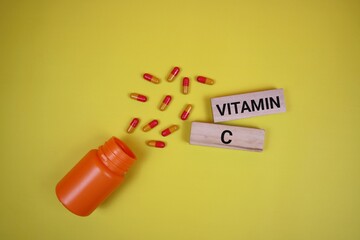 Colorful vitamin C capsules scattered from an orange bottle, placed on a yellow background
