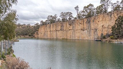 Serene quarry lake panorama framed by imposing cliffs and lush foliage under cloudy skies