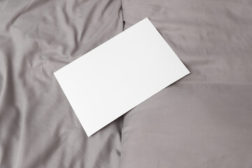 White blank paper sheet lies on the bed sheet with pillows