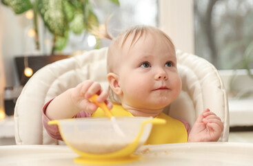 Cute little baby girl eats on her own at the feeding table