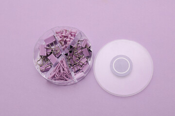 Set of purple paper clips, binders and pins  with box on lavander background