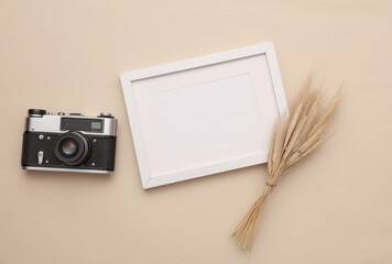 Mockup of white photo frame with dry grass and film camera on beige background