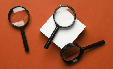 White square memo papers with a magnifying glasses on a red background