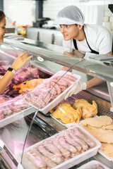 Knowledgeable male butcher proudly showcases finest cuts on his stand, guiding customer's choice.