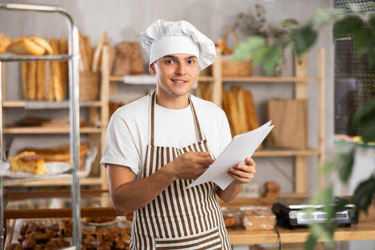 Thrilled entrepreneur in green apron reacting with excitement while reviewing financial documents showing increased profits in small artisan bakery - Powered by Adobe