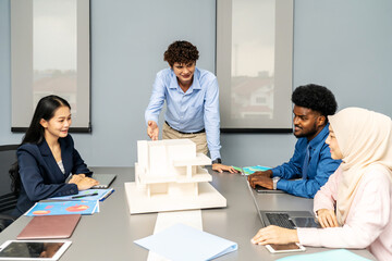 Architects and designers work presenting and discussing house model in office meeting. The participants are engaged in an in-depth conversation, Experts look at model homes and architectural drawings