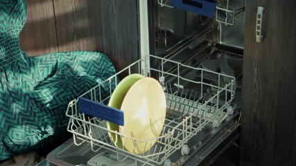 Woman taking plates out of modern dishwasher in home kitchen . Daily routine