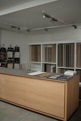 Empty showroom interior featuring wooden counter displaying various tile and flooring samples, shelving units in background holding multiple material swatches and sample boards