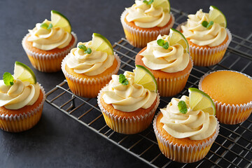 Several delicious cupcakes with light yellow frosting and lime slices are arranged on a cooling rack.