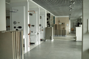 Modern showroom displaying various bathroom fixtures and shower installations with multiple tile samples arranged in foreground, no people visible, spacious commercial interior