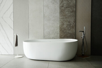Modern freestanding bathtub standing in front of textured stone wall panels with floor mounted faucet and towel holder, empty bathroom interior emphasizing clean minimalist design