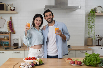Smiling couple holding fresh orange juice glasses together in modern kitchen with healthy food lifestyle