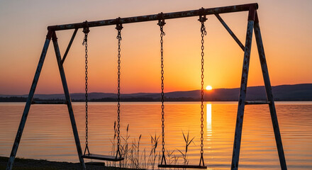 Serene sunset over calm lake with empty swings evokes peaceful reflection and childhood memories