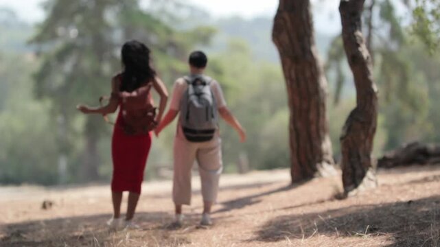 Young multi ethnic couple hiking together on sunlit forest trail, wearing backpacks and sharing intimate moments during summer vacation