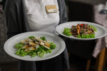 A waiter holding two plates of gourmet salads in a restaurant.