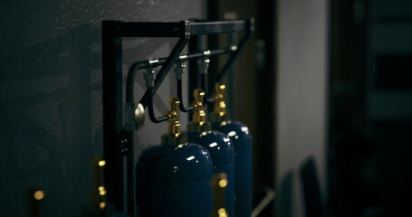 A row of blue gas cylinders is prominently displayed on a sturdy metal rack. The dim lighting creates a mysterious atmosphere, highlighting the industrial nature of the workshop environment.