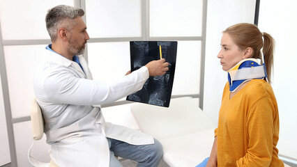 Obraz premium Adult woman with neck injury in a cervical brace during consultation with manual therapist who is looking at MRI of patient's neck