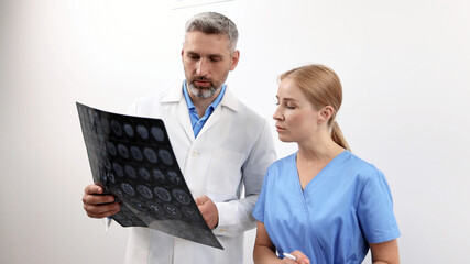 Two healthcare specialists closely examine brain MRI scans in a medical facility, discussing findings and planning appropriate treatment options for a patient