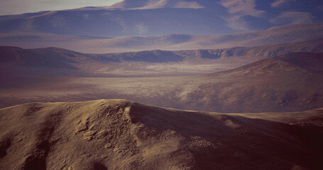 Vast desert terrain stretches into the distance, showcasing rolling hills and rugged mountains that capture the warm hues of sunset. The atmosphere is serene and untouched.