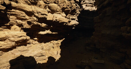 Visitors navigate through a narrow canyon during midday, as sunlight streams in from above, highlighting the rugged rock formations and shadows cast on the ground.
