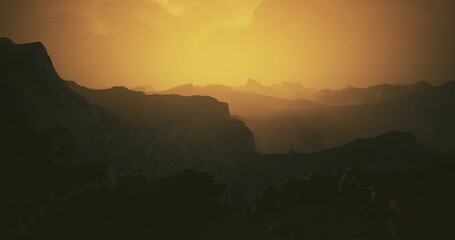 Obraz premium A breathtaking view of rugged mountains illuminated by the warm glow of sunset. The landscape features deep valleys and silhouettes against the vibrant sky, creating a serene atmosphere.