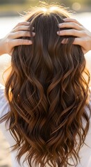 Obraz premium Woman with beautiful, wavy brown hair, enjoying the warm sunlight on her head, outdoors.