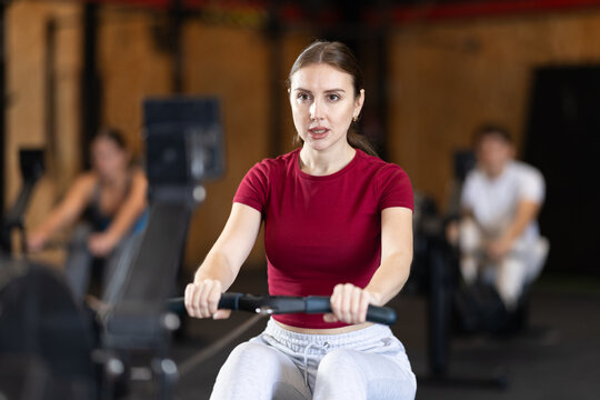 Woman is a client of the fitness room working out on a rowing machine.