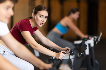 Young woman during an intense workout on an exercise bike in the gym. Woman sweating and doing...