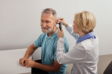 Senior man during ear test with audiologist at audiology. Diagnosis of impairment and hearing testing to senior people, otoscopy