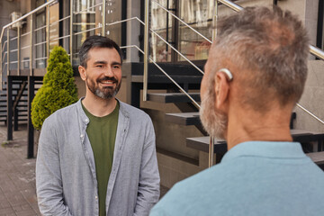 Two friends chat in a busy city, using a hearing aid for clear communication amid the noise
