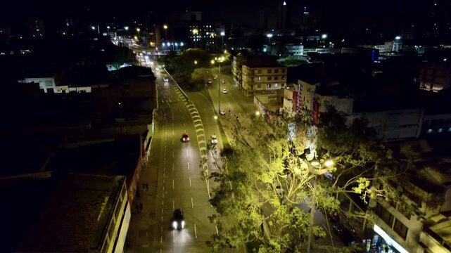 Night drone aerial view of Cali Valle del Cauca Colombia featuring Calle 5 with glowing streetlights, moving cars and surrounding urban landscape.