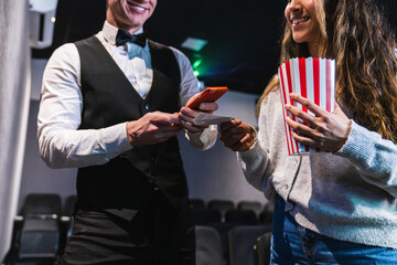 Smiling usher scanning movie ticket of a young woman holding popcorn bucket in a movie theater
