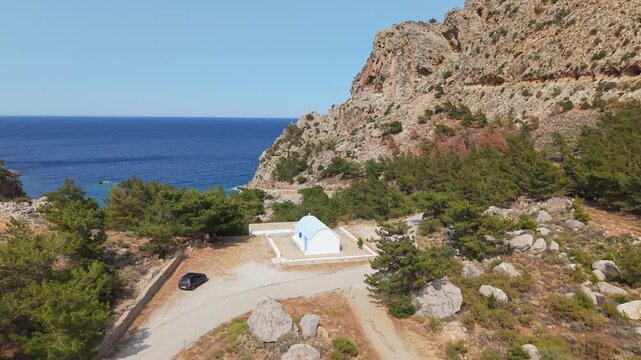 Drone orbit and ascend from a hilltop chapel revealing the scenic Achata Beach in Karpathos, Greece.