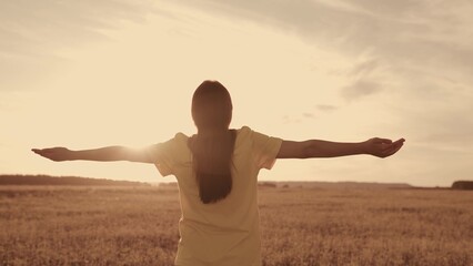 girl with hands raised dreamily meditates sunset. girl's hands rays sun glare. female dream...