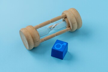 A wooden hourglass and a blue cube with the male symbol. Male health, andropause, aging concept....