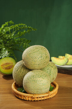 Fresh Hainan Honeydew Melons with Reticulated Skin in Wicker Basket on Wooden Kitchen Table