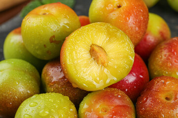 Fresh Ripe Plums with Water Droplets Cut in Half Showing Juicy Yellow Flesh in Wooden Bowl