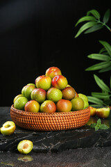 Fresh Ripe Plums in Wicker Basket on Dark Background with Green Leaves