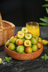 Fresh Ripe Plums in Wicker Basket with Orange Juice on Dark Slate Background