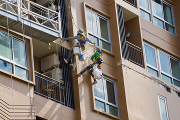 Two workers in safety gear perform maintenance on high rise building facade, using ropes and harnesses for support