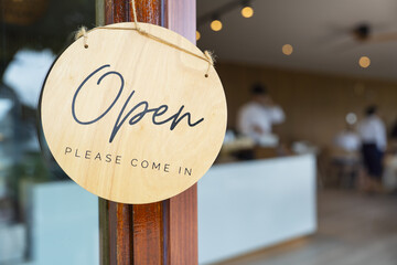 Open sign on wooden door invites customers into cozy cafe with blurred interior